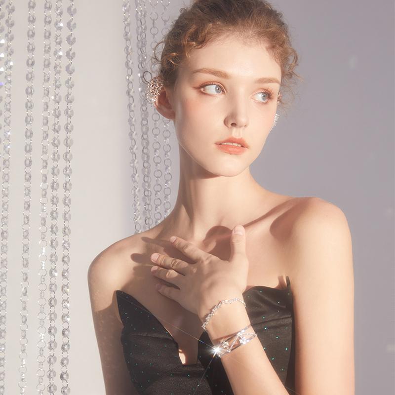 Elegant woman in black dress wearing sparkling statement bracelet and ear cuff, with crystal curtain backdrop