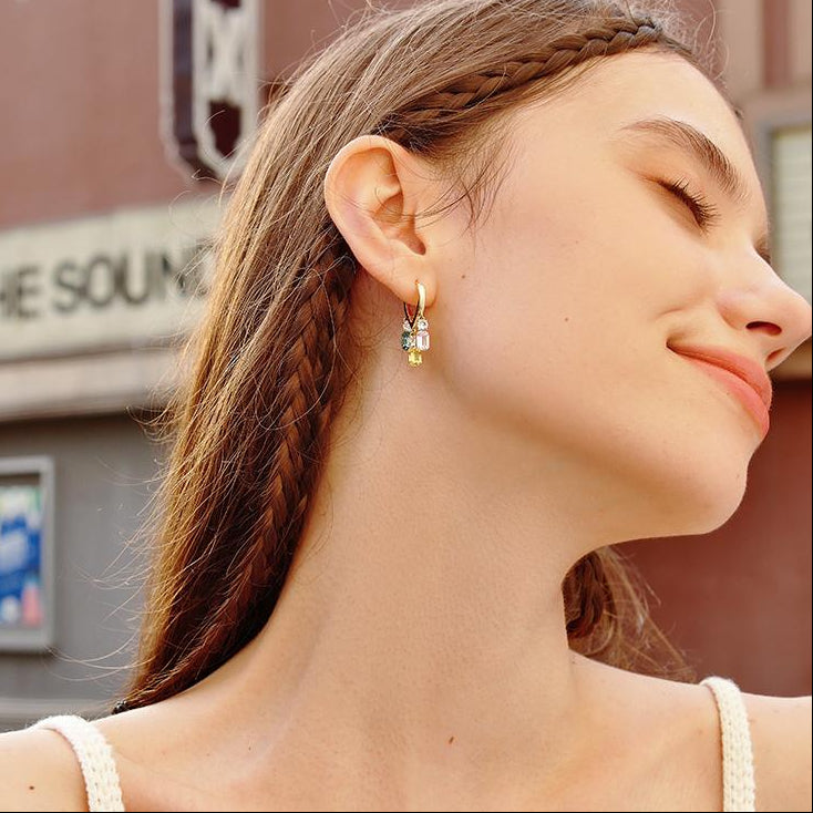 Woman wearing gold-plated hoop earrings with colorful gemstone charms outdoors