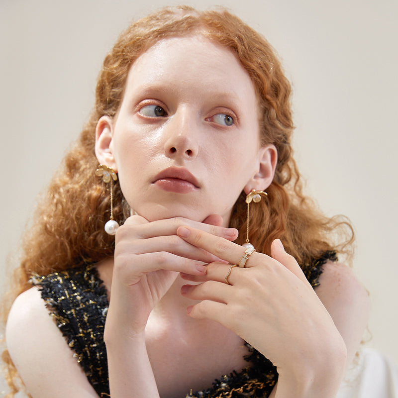 Woman wearing gold-plated statement earrings with pearl and elegant rings