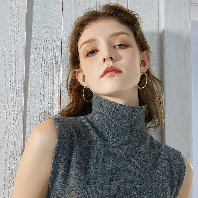 Woman wearing gold-plated hoop earrings and a grey sleeveless turtleneck sweater