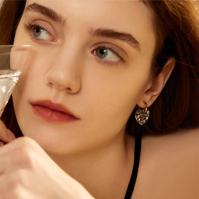 Woman wearing gold-plated heart-shaped statement earrings with sparkling stones