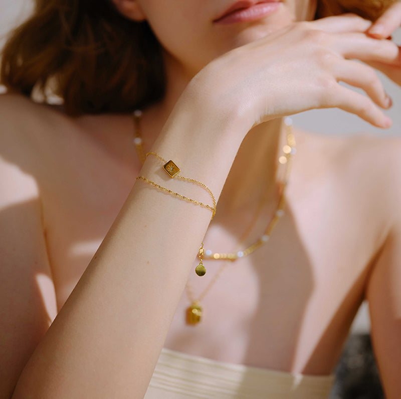 Woman wearing layered gold-plated bracelet and pendant necklaces in natural light