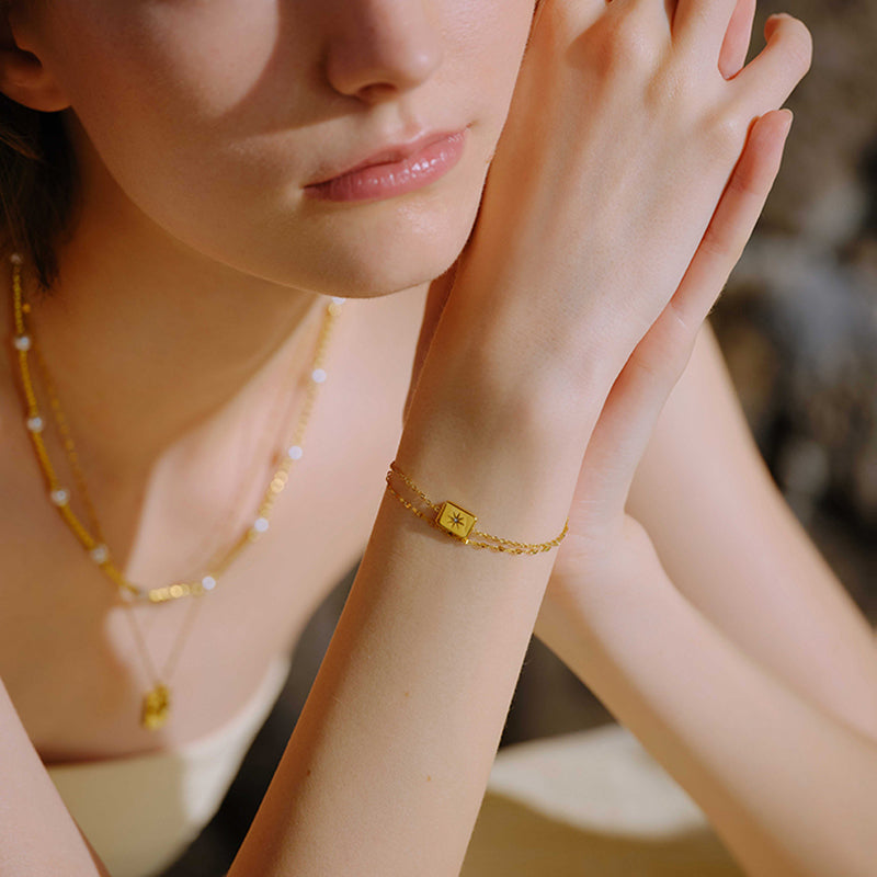 Woman wearing gold-plated star charm bracelet and layered gold necklace with pearls