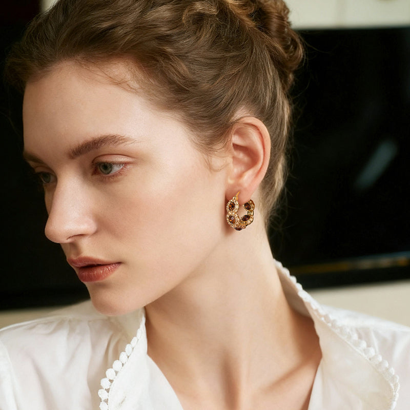 Woman wearing gold-plated hoop statement earrings with gemstones, elegant style