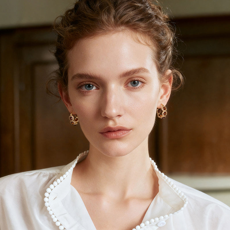 Woman wearing gold-plated statement earrings and a white blouse with pearl trim