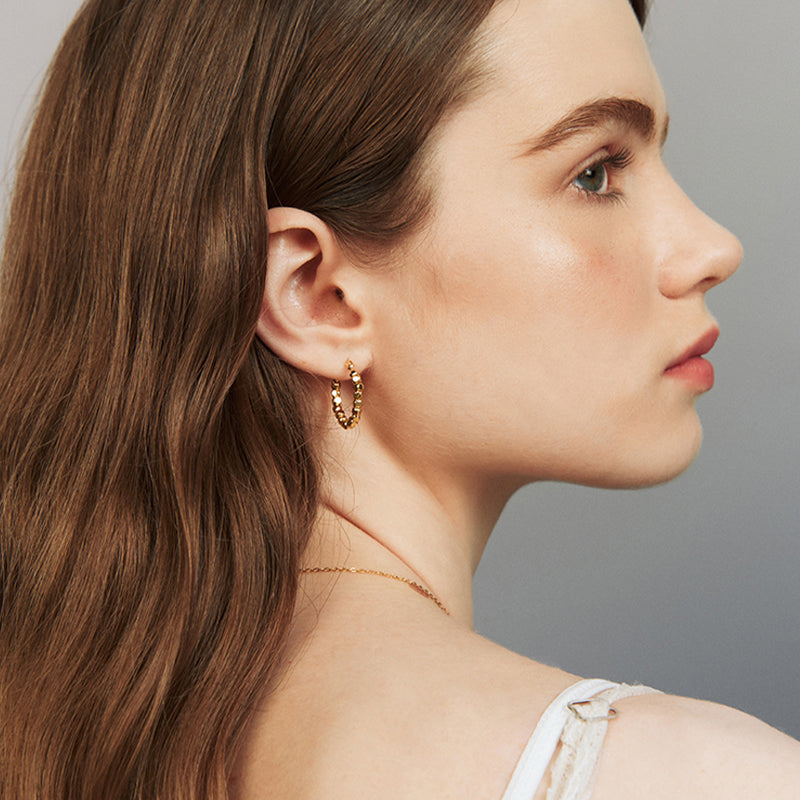 Woman wearing gold-plated twisted hoop earrings and a delicate gold chain necklace