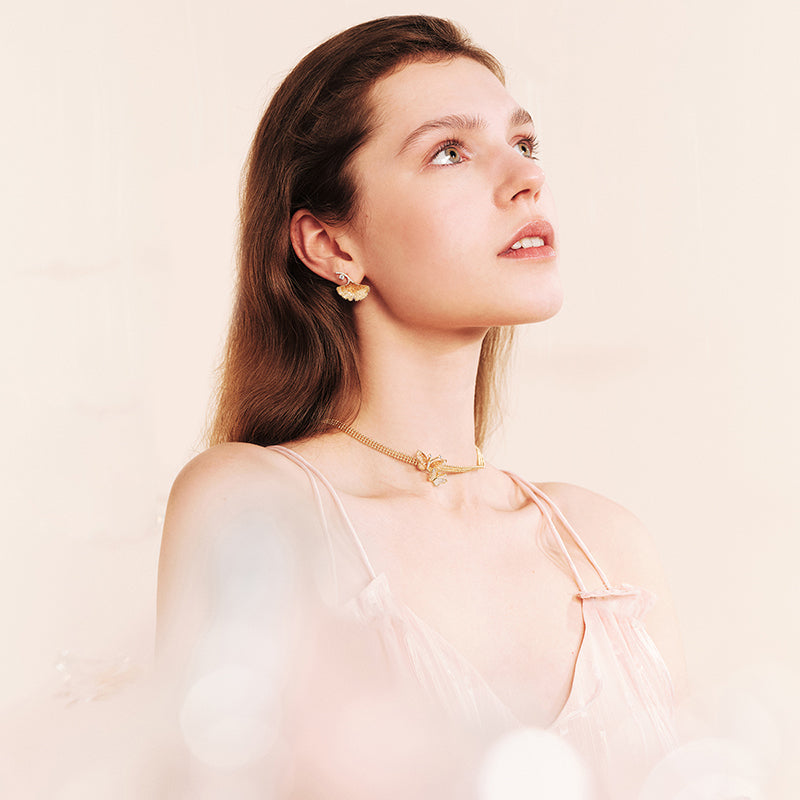 Woman wearing gold-plated butterfly necklace and earrings, soft pink dress, elegant style