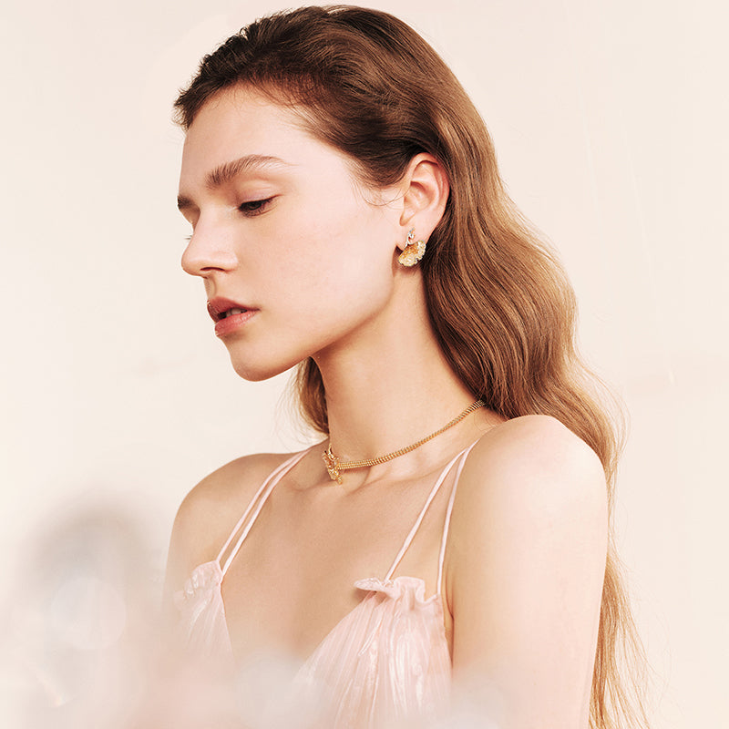 Woman wearing gold-plated statement earrings and elegant gold necklace in soft lighting