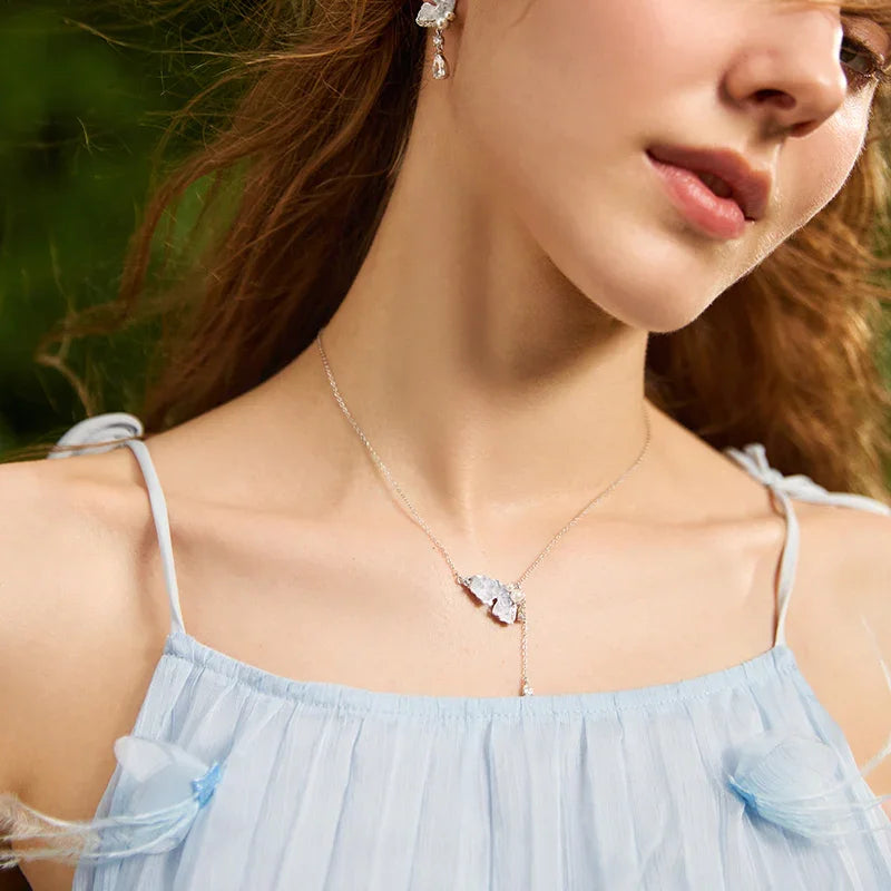 Woman wearing a delicate silver necklace with a crystal pendant and matching drop earrings
