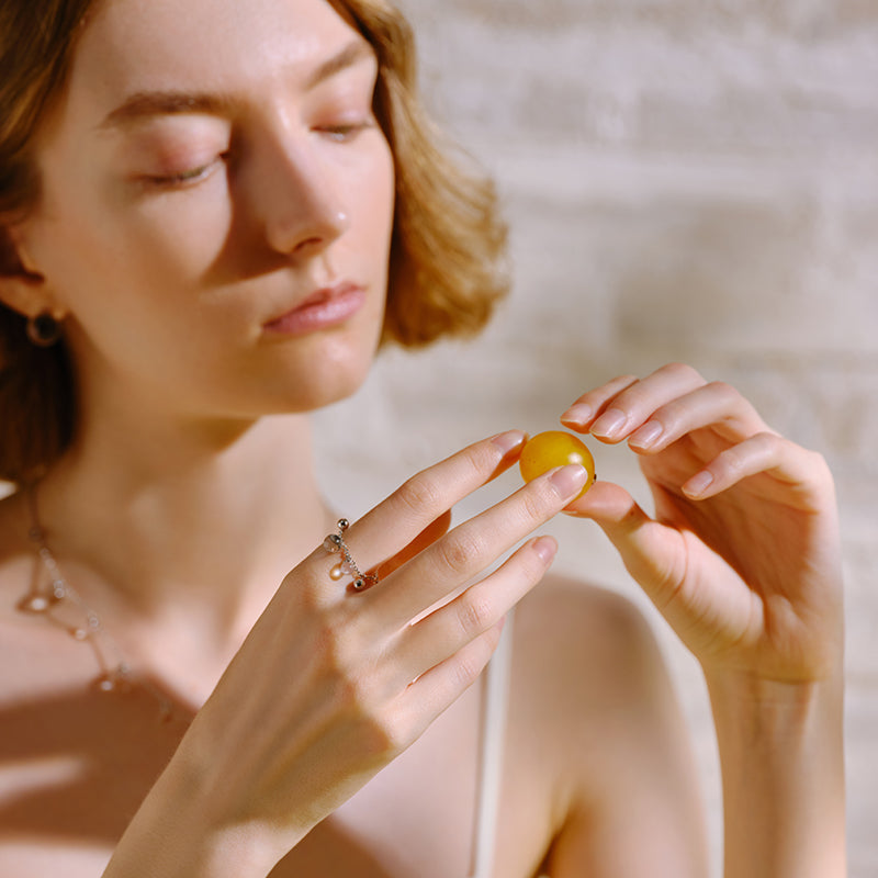 Woman wearing a silver pearl statement ring and necklace, holding a yellow grape
