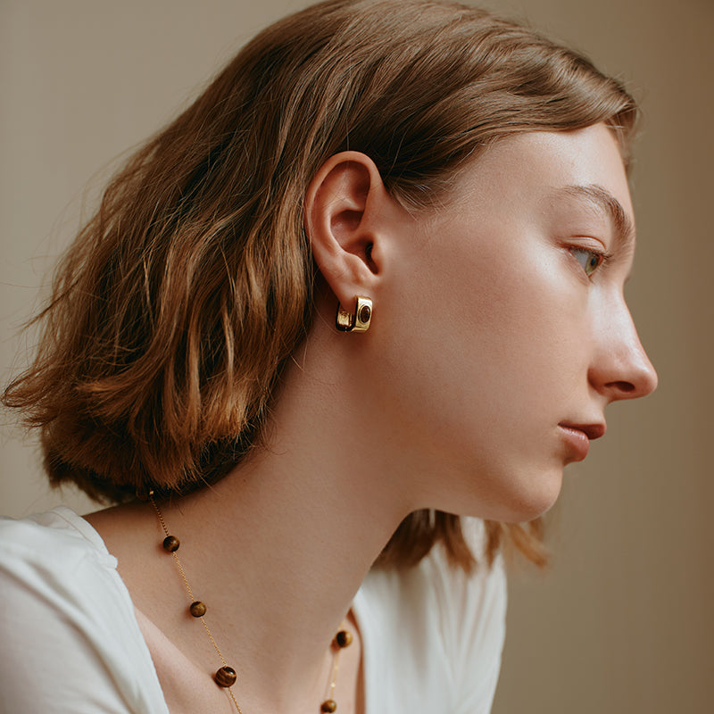 Woman wearing chunky gold-plated hoop earrings and a beaded gold necklace
