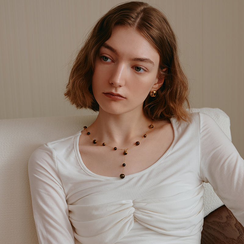 Woman wearing a gold-plated beaded necklace and statement earrings, white ruched top