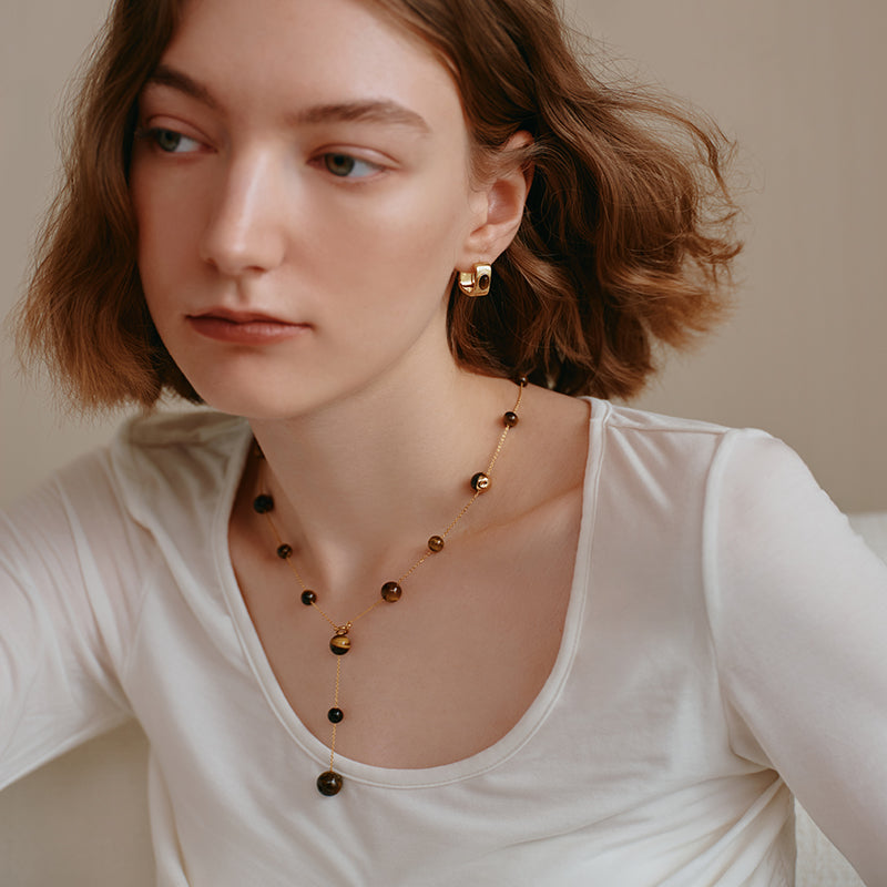 Woman wearing gold-plated statement earrings and a beaded lariat necklace with brown stones