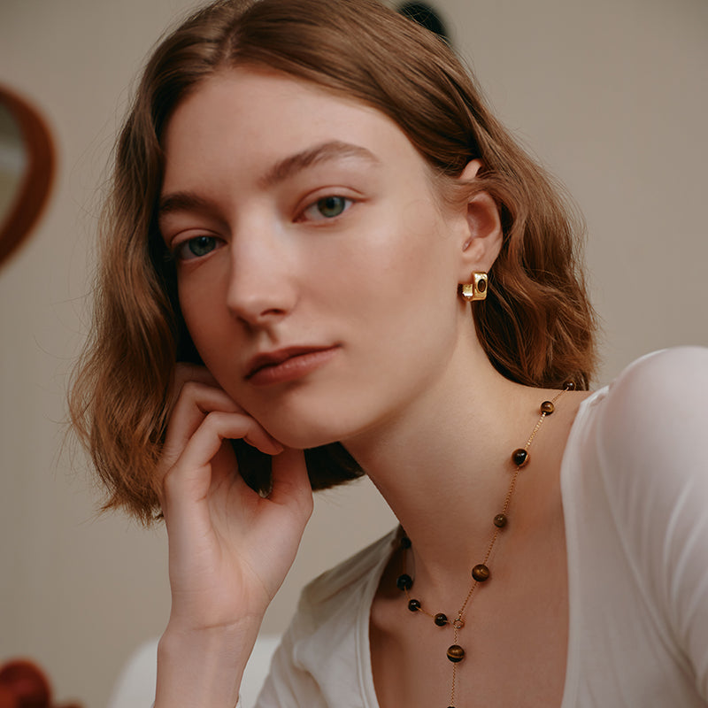 Woman wearing gold-plated statement earrings and beaded necklace, close-up