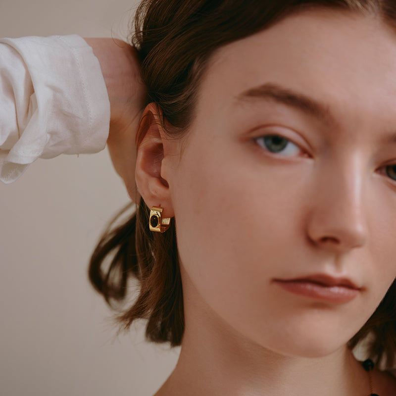 Woman wearing gold-plated geometric statement earring, close-up portrait.