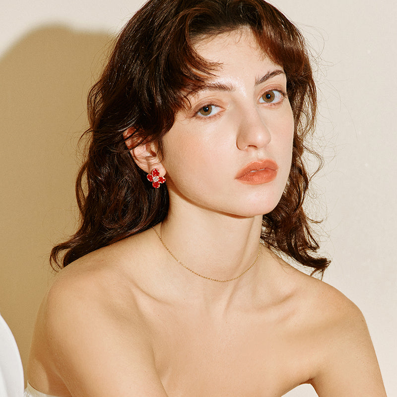 Woman wearing gold-plated necklace and red floral statement earrings