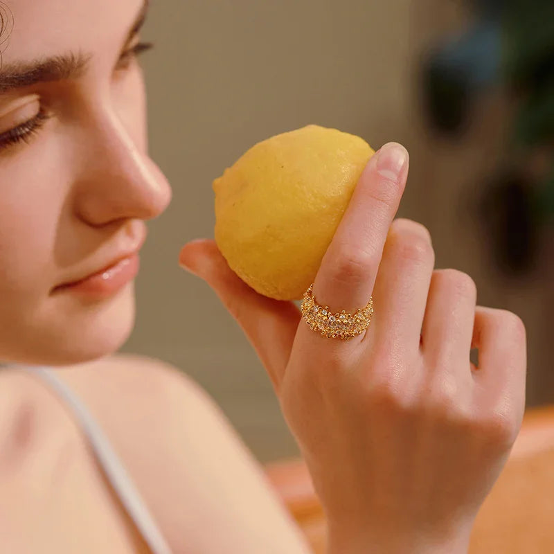 Woman wearing a gold-plated crystal ring holding a lemon, close-up jewelry detail