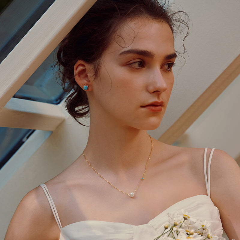 Woman wearing a gold-plated necklace with pearl pendant and turquoise stud earrings