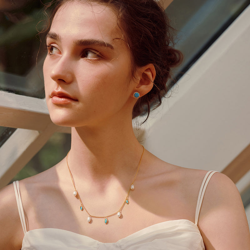 Woman wearing gold-plated necklace with pearl and turquoise accents, matching turquoise stud earring