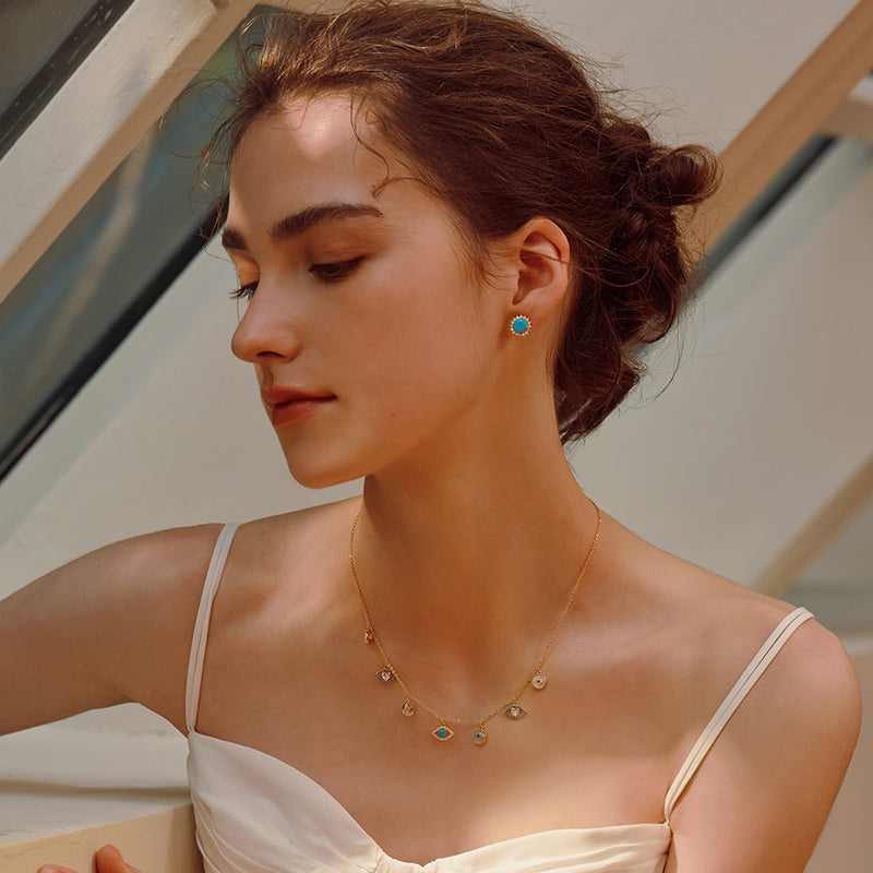 Woman wearing gold-plated gemstone necklace and turquoise stud earrings in natural light