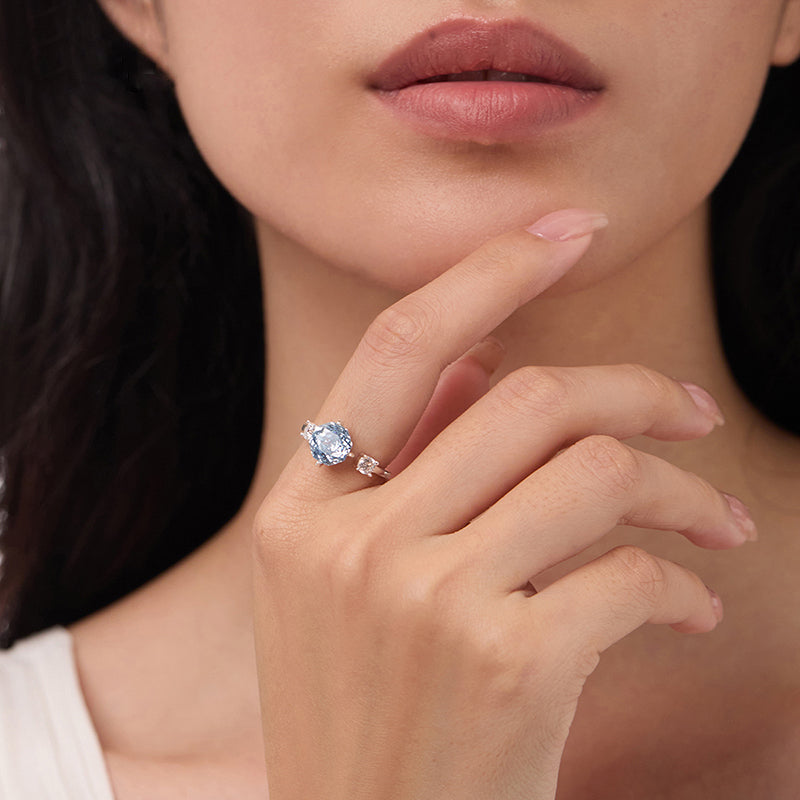 Woman wearing a gold ring with large blue gemstone and clear crystal accents