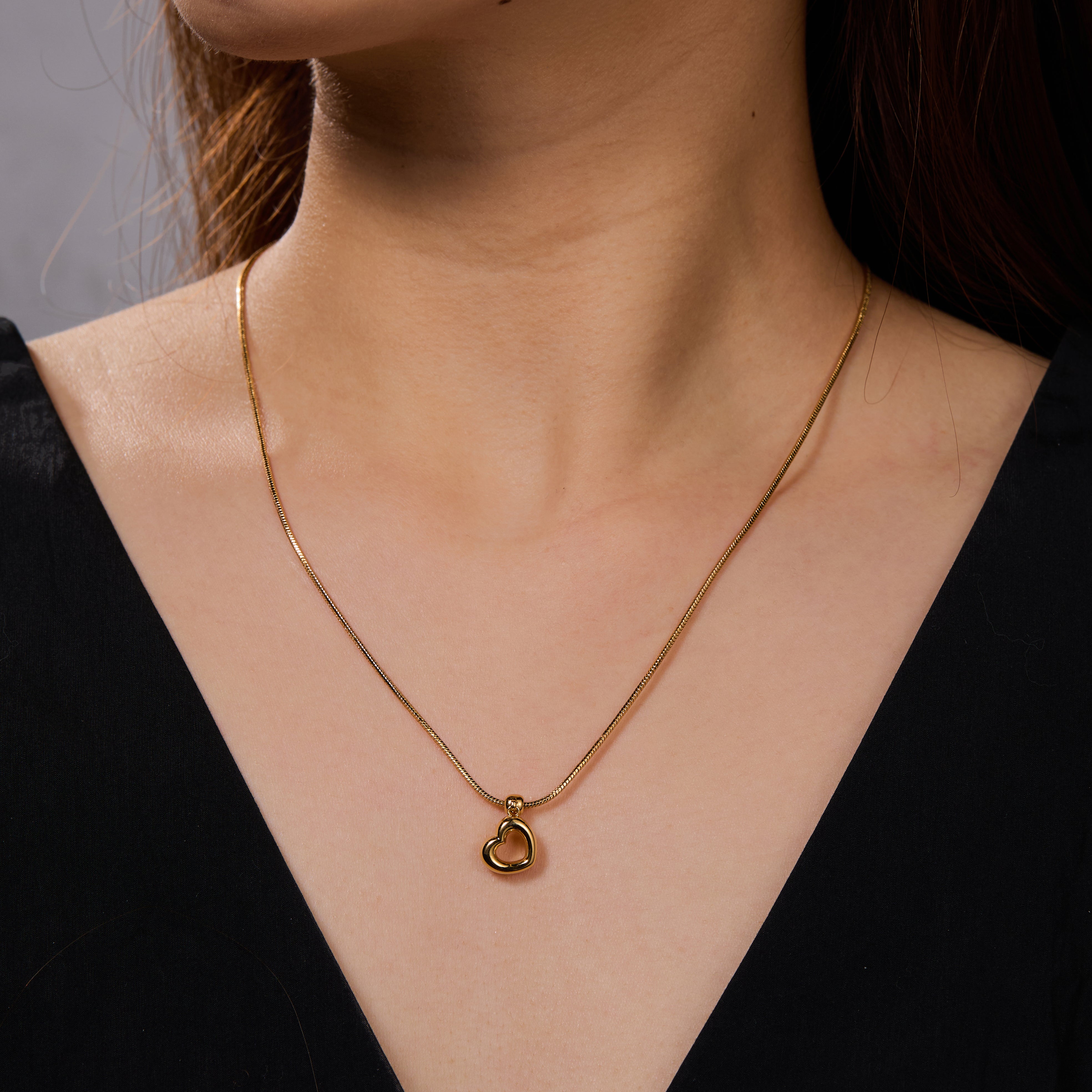 Gold-plated heart pendant necklace on woman in black v-neck top