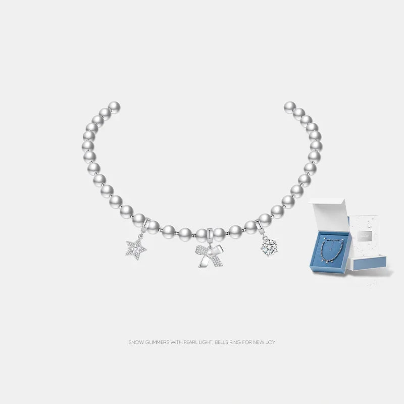 Silver beaded necklace with star, bell, and snowflake charms, shown with gift box