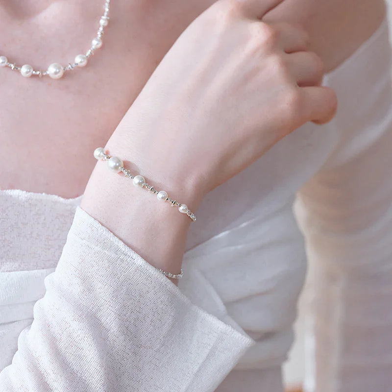 Woman wearing a delicate pearl bracelet and matching pearl necklace, dressed in white.