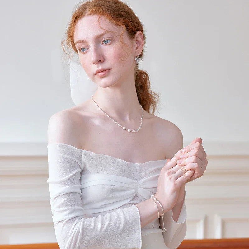 Woman in white off-shoulder dress wearing pearl necklace, earrings, and bracelet