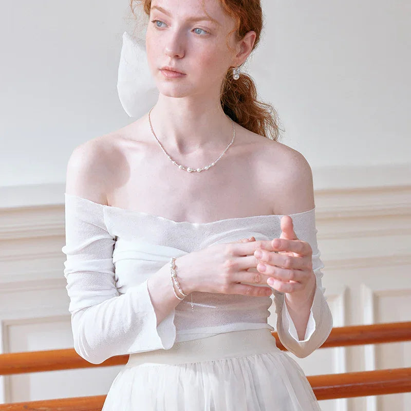 Woman in off-shoulder white dress wearing pearl necklace, bracelet, and earrings.